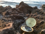 A close-up of a compass resting on a sandy beach.