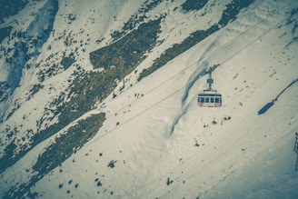 Dynamic shot of a cable car gliding over snowy alpine terrain during sunset.
