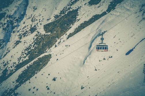 Dynamic shot of a cable car gliding over snowy alpine terrain during sunset.