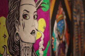 A stylized, graphic illustration of a person with exaggerated features, including large eyes and decorative tattoos. There is smoke rising from the corner of the mouth. The background features vibrant colors like pink and yellow, with abstract patterns and designs.