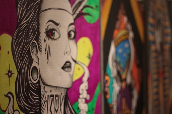 A stylized, graphic illustration of a person with exaggerated features, including large eyes and decorative tattoos. There is smoke rising from the corner of the mouth. The background features vibrant colors like pink and yellow, with abstract patterns and designs.