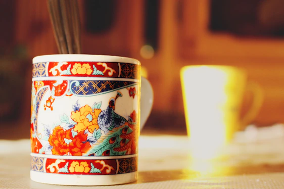Close-up of vibrant, hand-thrown ceramic mugs resting on a cozy wooden table bathed in soft natural light.