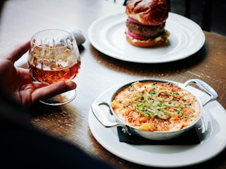 person holding clear snifter beside bowl of soup