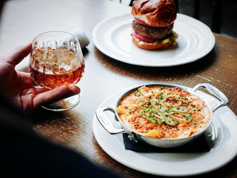 person holding clear snifter beside bowl of soup