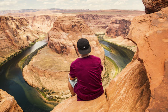 man sitting on brown mountain located at Grand Canyon during daytime
