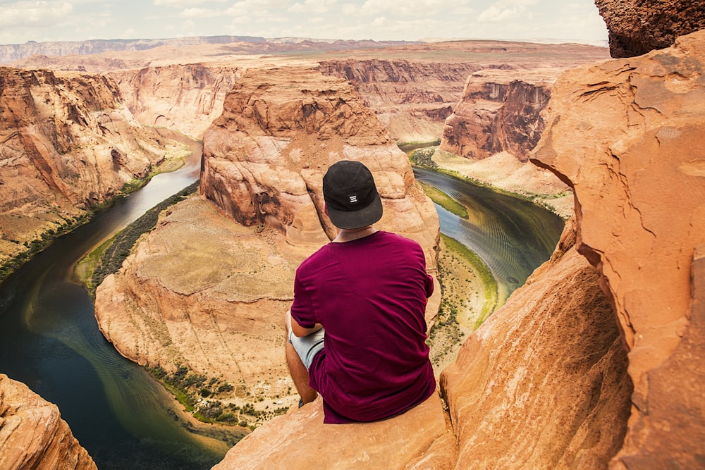 uomo che si siede sulla montagna marrone situato al Grand Canyon durante il giorno