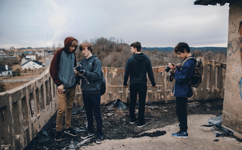 four man wearing blue jackets standing beside house looking at their cameras during daytime