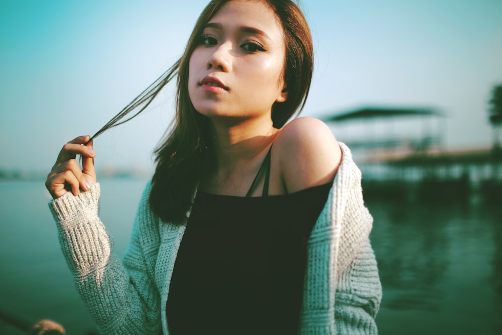 selective focus photo of woman holding string of hair near body of water during daytime