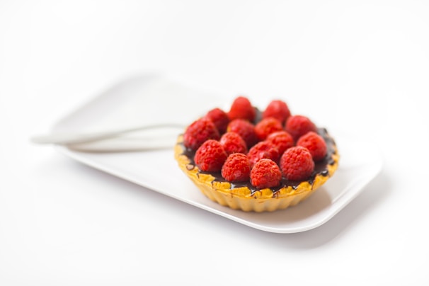 A colorful raspberry tart topped with fresh raspberries and mint leaves on a wooden board.