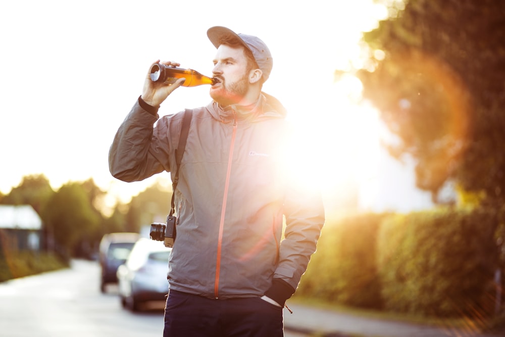 グレーとピンクのジップアップパーカーを着た男が昼間に飲んでボトルを持っている