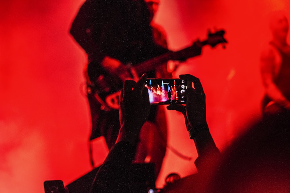 person holding smartphone in front of a person playing guitar on stage