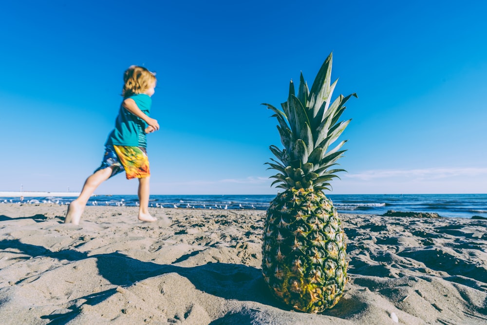 selektives Fokusfoto von grüner und gelber Ananas in der Nähe eines rennenden Kindes, das ein blaues T-Shirt-Foto trägt, das tagsüber aufgenommen wurde