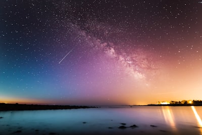 milky way above body of water star teams background