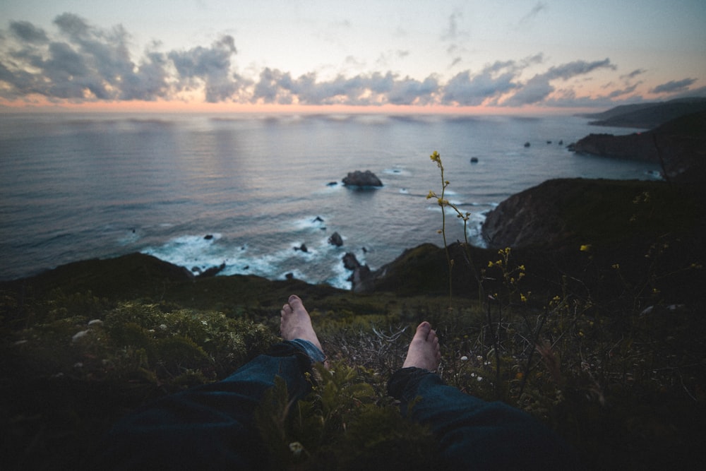 man sitting on green grass near body of water