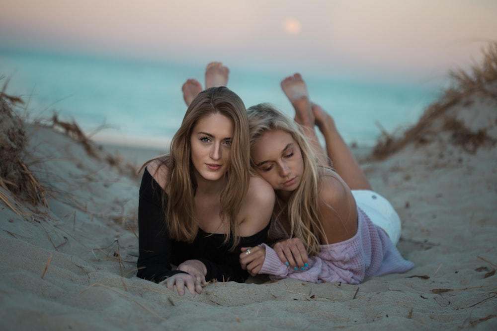 two woman lying on sand facing camera