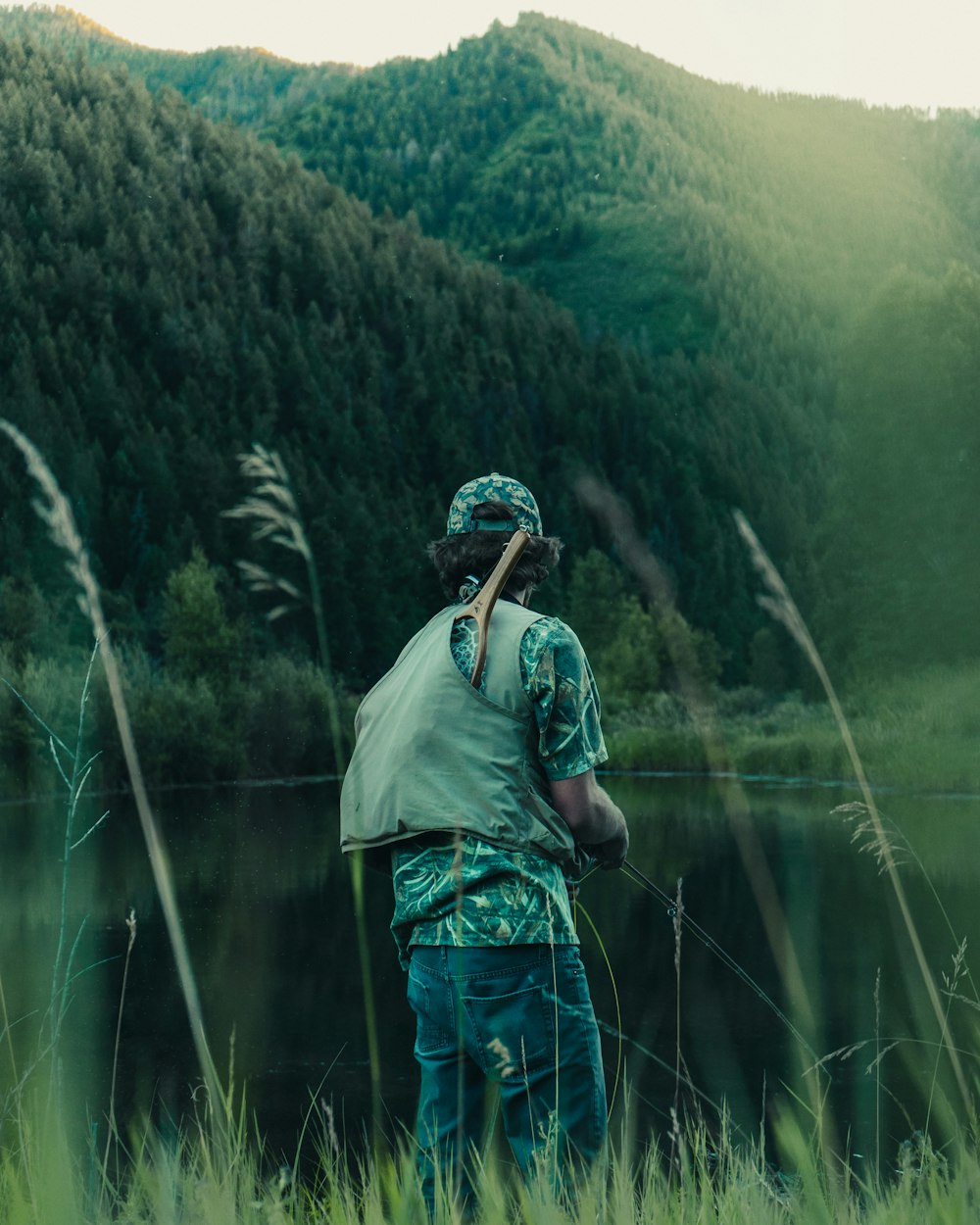 person fishing on body of water near mountain during daytime