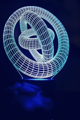 A complex geometric structure composed of interwoven loops outlined by a thin, glowing blue grid against a dark background.