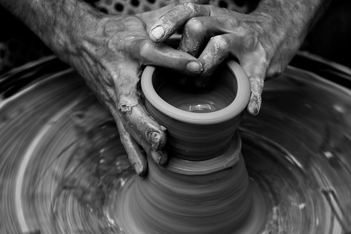 Black and white photo of a pair of hands molding a vessel on a pottery wheel