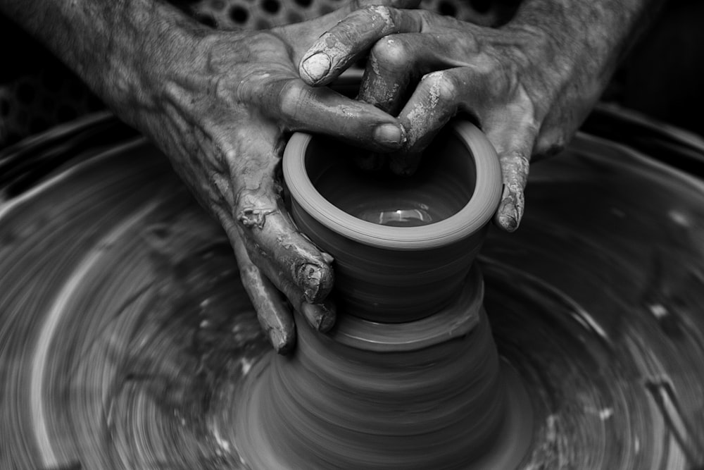 Mãos bagunçadas esculpindo em uma roda de cerâmica em movimento