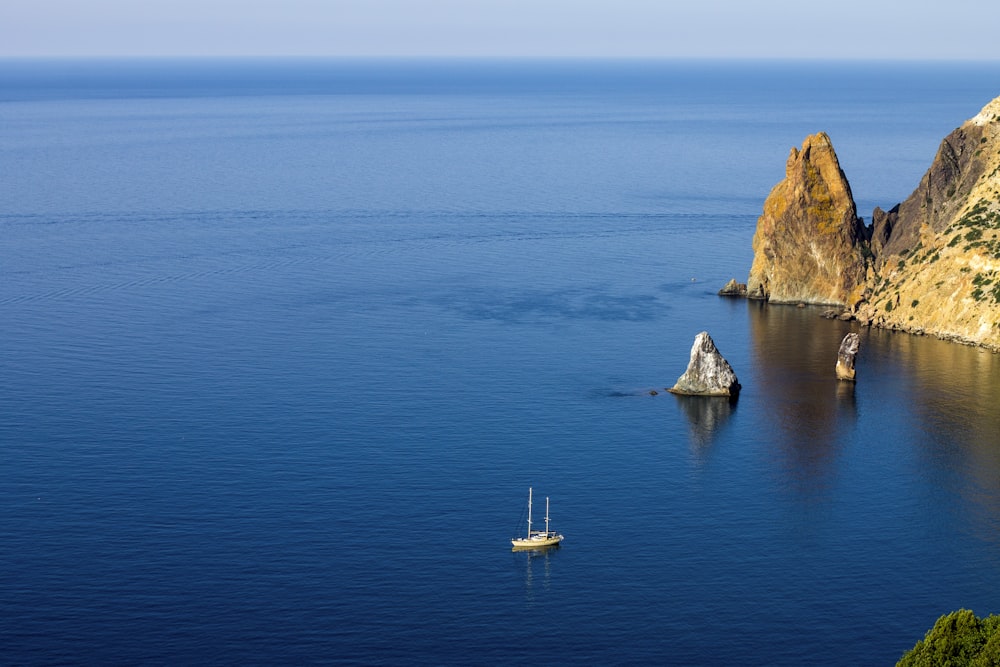 Fotografía aérea de un barco blanco en el mar cerca de formaciones rocosas bajo el cielo azul durante el día