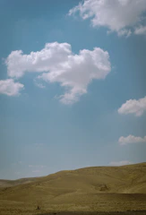 An expansive desert landscape under a vast blue sky with scattered clouds.