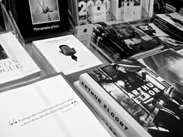 A display of various photography books is spread across a table, each featuring monochrome covers and titles prominently displayed. The arrangement includes a stack of Herb Ritts books with a distinct profile image on the cover, an Arthur Elgort book with vibrant, expressive imagery, and other photography-related literature. The overall aesthetic is clean and sophisticated, emphasizing visual artistry.