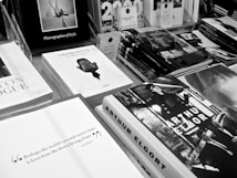 A display of various photography books is spread across a table, each featuring monochrome covers and titles prominently displayed. The arrangement includes a stack of Herb Ritts books with a distinct profile image on the cover, an Arthur Elgort book with vibrant, expressive imagery, and other photography-related literature. The overall aesthetic is clean and sophisticated, emphasizing visual artistry.