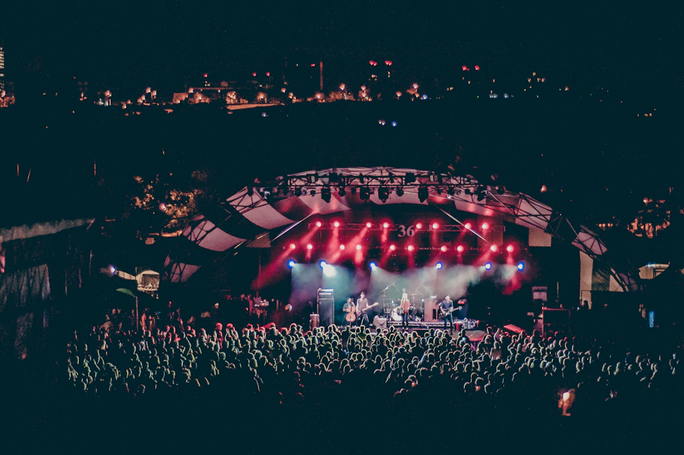 Crowd gathered at an outdoor concert with the city skyline glowing behind