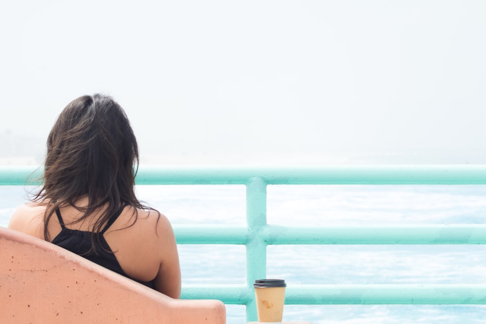 Woman sitting alone with cup of coffee behind light blue railing at Manhattan Beach