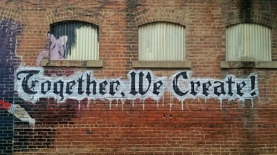graffiti tag on brown brick wall, stating 'Together, We Create!'