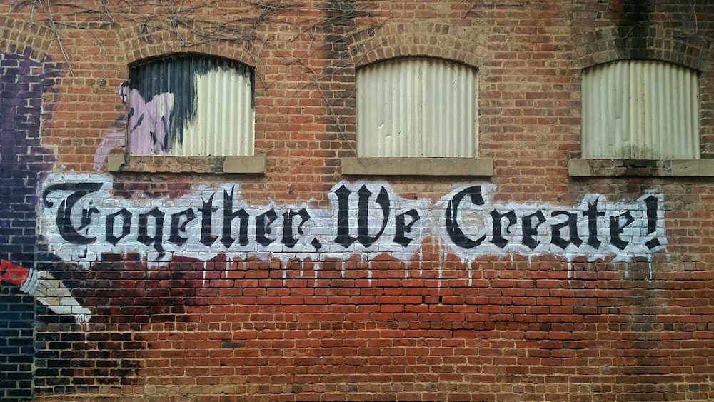 Graffiti words read "Together, we create!" below small windows on a brick wall