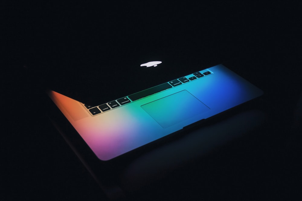 The screen of a half-closed MacBook illuminating the keyboard with various colors