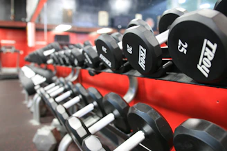 A row of sleek, black weightlifting machines with bright red accents under bright gym lighting.