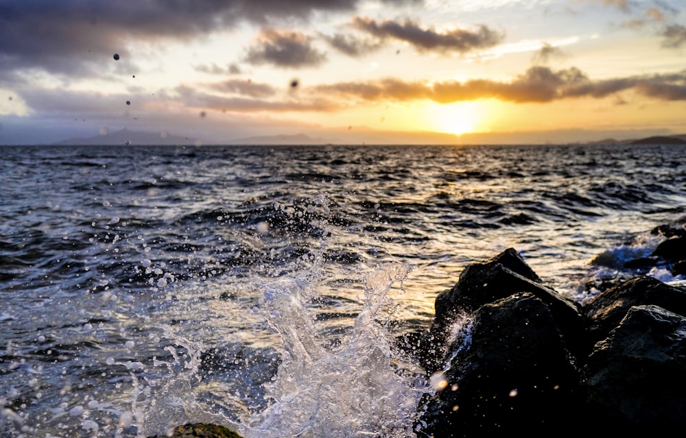 fotografía de enfoque superficial de la orilla del mar con las olas bajo la puesta de sol naranja