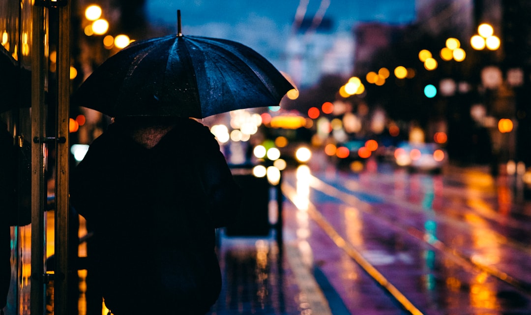 person walking on street while holding black umbrella near cars on road at nighttime