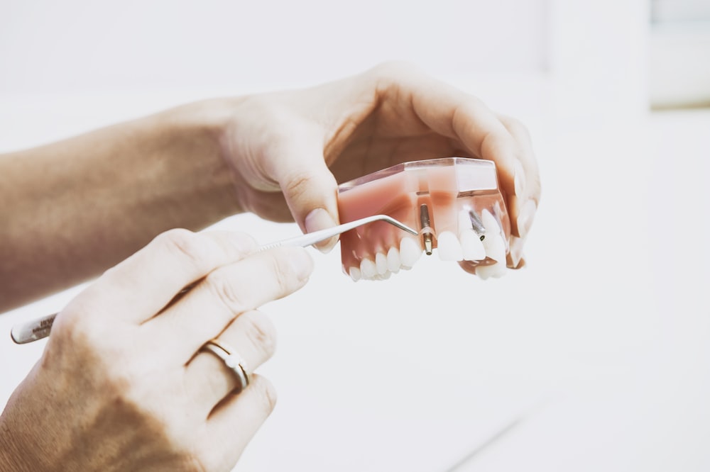 person wearing silver-colored ring while holding denture pointing at area where people should floss their teeth.