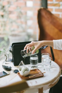 person pouring green liquid on ice cream on scalloped-edge white ceramic bowl
