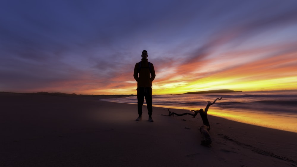 homme debout sur une plage au coucher du soleil