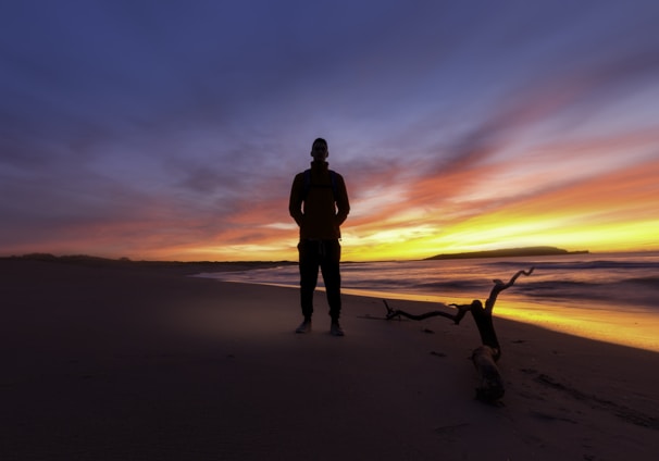 man standing on a beach during sunset