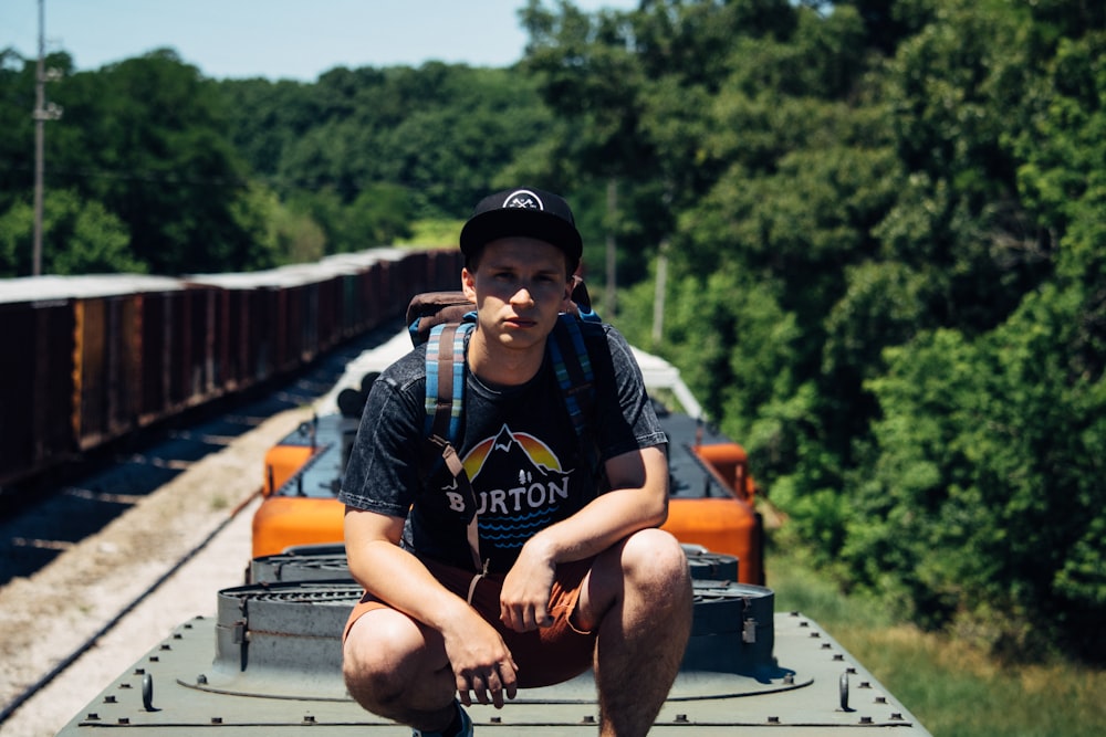 man with backpack sitting on gray platform surrounded by trees during daytime