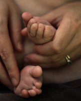 A close-up of hands gently holding a baby’s tiny feet, symbolizing trust and care.