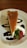 A slice of cheesecake topped with a smooth layer of caramel is elegantly placed on a white plate. It is accented with swirls of chocolate sauce, a dollop of whipped cream, and a fresh strawberry.