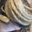 A close-up view of a coiled rope made of natural fibers, possibly sisal or jute, with a soft bristle paintbrush partially visible near it. The rope has a tightly wound texture, and the brush handle appears to be wooden.