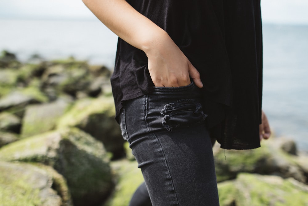 persona che indossa pantaloni di jeans neri vicino allo specchio d'acqua durante il giorno