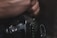 A person is holding a Canon film camera with a focus on the lens and intricate details, surrounded by a soft, dark background.