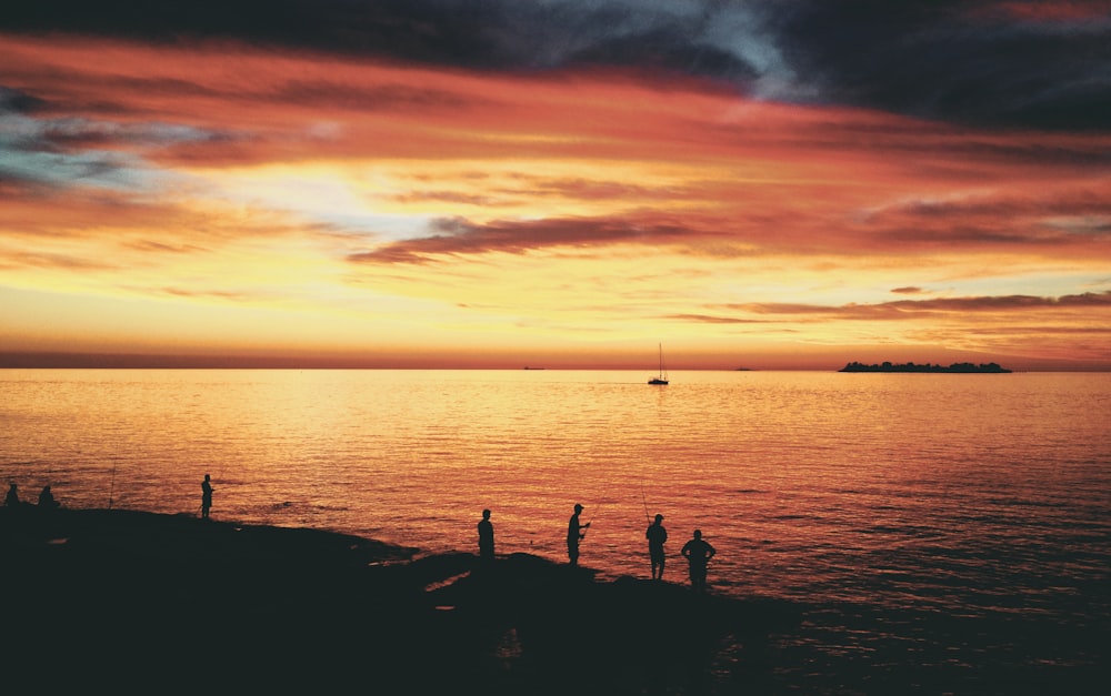 silhouette photo of people near seashore during sunset