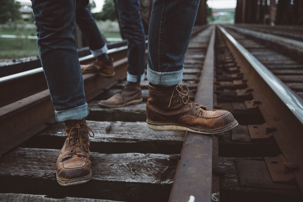 two people wearing brown shoes standing in train rail