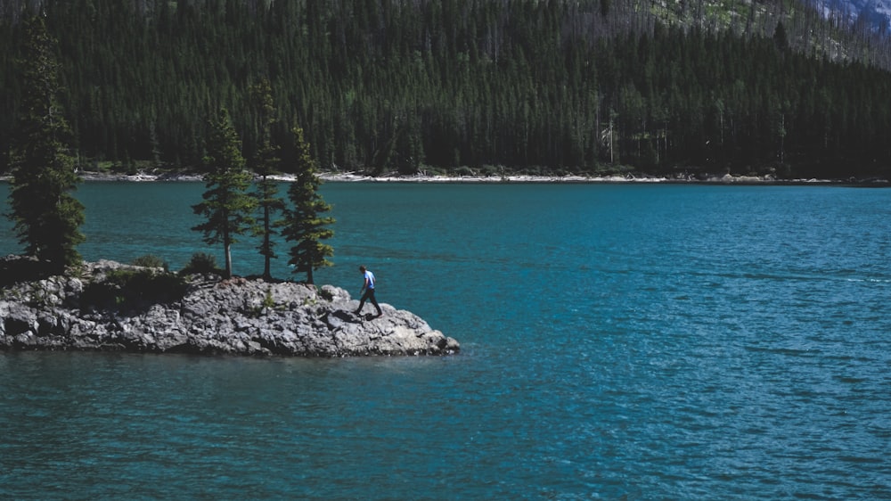 person walking on rock beside body of water