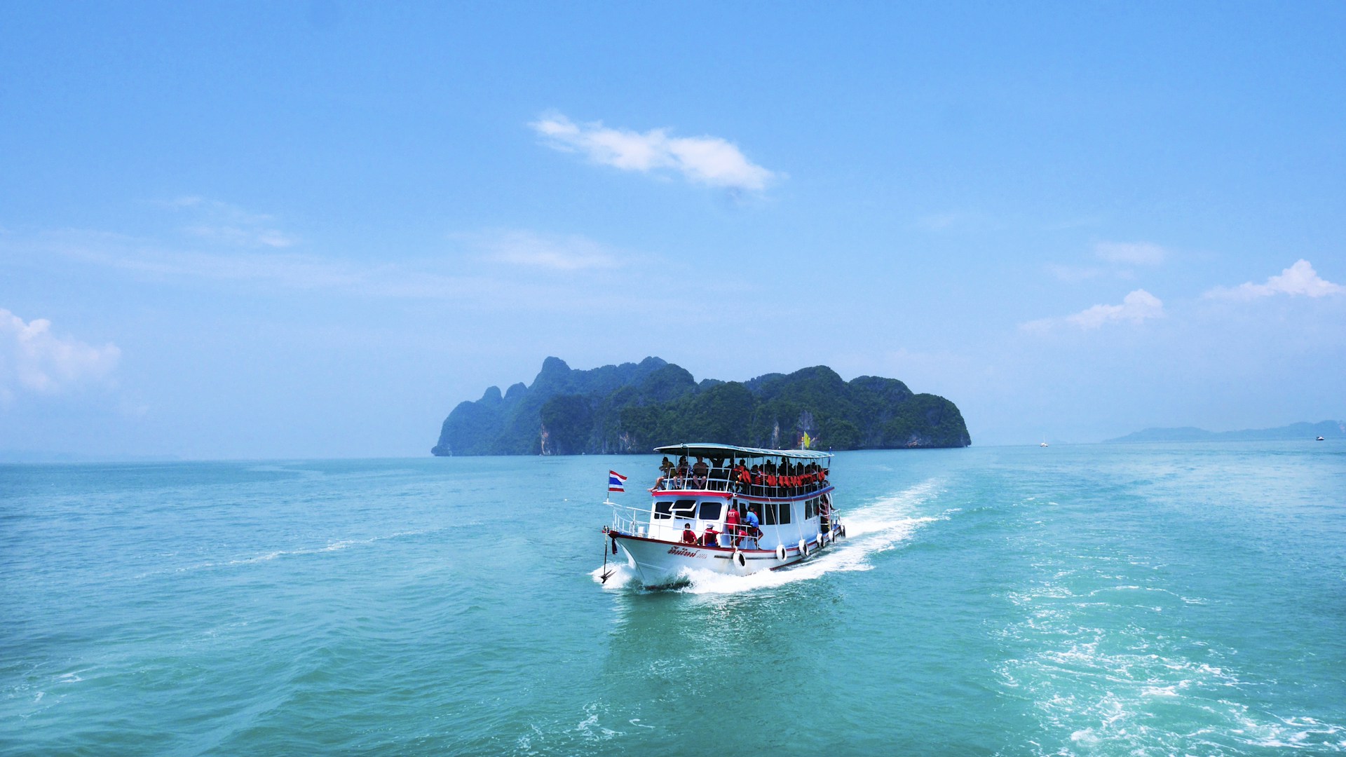 boat with peoples sailing on body of water with island background