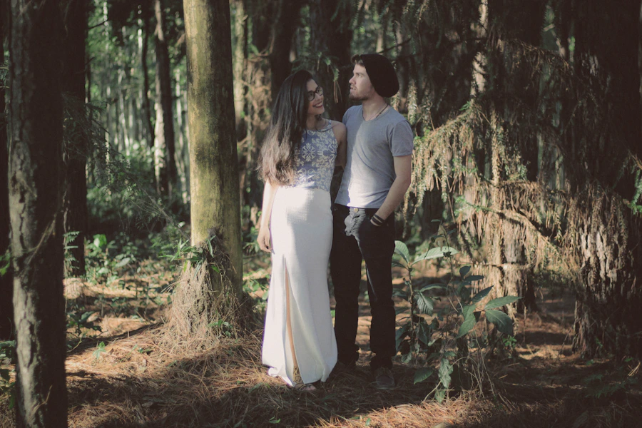 A stylish couple standing close together in a lush green forest setting